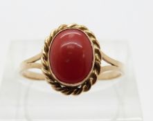 A 14ct gold ring set with a coral cabochon within a rope twist border,