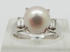 A platinum ring set with a pearl and with an emerald cut diamond to each shoulder, total diamond