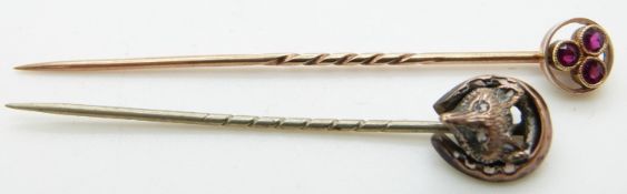 A gold stick pin set with three rubies and another stick pin in the form of a horseshoe and fox's
