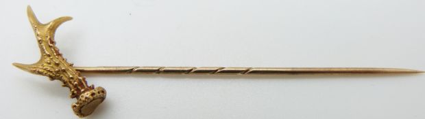 A yellow metal stick pin in the form of an antler with textured detail