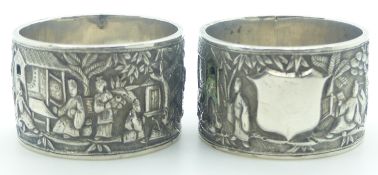 Pair of Chinese white metal napkin rings decorated with figures, buildings and trees, with Chinese