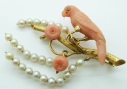 An 18ct gold brooch in the form of a parrot on a branch, the parrot carved coral set with a