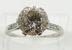A platinum ring set with a round cut diamond of approximately 2.7ct with diamond encrusted