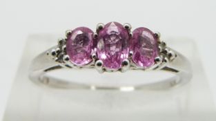 A 9ct white gold ring set with three oval pink sapphires and diamonds, size N
