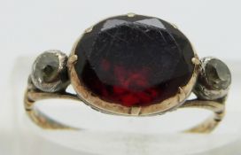 A Georgian ring set with a foiled garnet and an old cut diamond to each shoulder, size H
