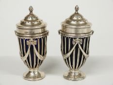 A pair of hallmarked silver pedestal peppers or casters with blue glass liners, swag decoration