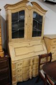 A blond oak serpentine fronted leaded glass door bureau bookcase