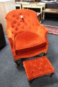 An Edwardian armchair in red/orange button fabric and a modern footstool