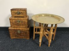 A circular folding brass topped table together with a set of three graduated oriental style caskets