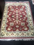 A fringed woollen Persian design rug on a red ground