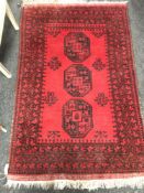 A fringed Afghan rug on red ground