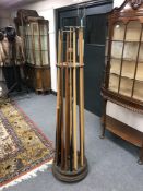 An early 20th century oak revolving snooker cue stand, together with sixteen various cues.