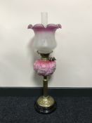 An early 20th century brass oil lamp with pink glass shade