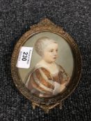 A gilt-framed oval portrait miniature depicting a young child sporting a bonnet and holding an