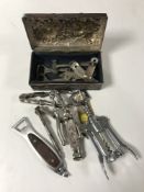 A copper embossed tin containing a collection of assorted bottle openers, nut crackers etc.