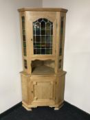 A blond oak corner display cabinet with stained leaded-glass door