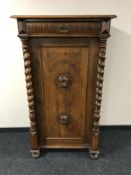 An early 20th century oak cabinet with a carved panel door and pillar supports,
