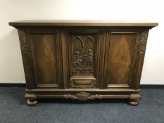 An early 20th century oak triple door sideboard with a carved panel door on bun feet