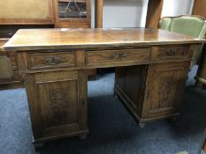 An early 20th century oak pedestal desk with carved panel doors