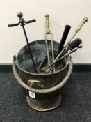 A large copper coal bucket containing fire irons and brushes