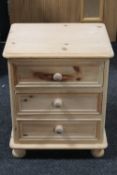 An unfinished pine three drawer bedside chest