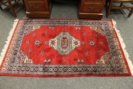 A fringed Indian rug on red ground,