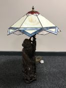 A carved wooden lamp base modelled as a Chinese elder with staff with a leaded glass shade