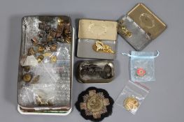 A tin containing a collection of military badges, buttons, patch,