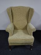 A wing back armchair upholstered in sand coloured fabric