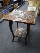 A heavily carved two tier occasional table