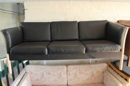 A wood framed black leather three seater settee