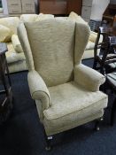 A wing back armchair upholstered in sand coloured fabric