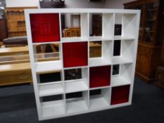 A set of white Ikea cube shelves together with four red perspex baskets