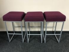 A set of three contemporary bar stools on metal legs upholstered in a purple fabric