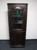 A carved oak corner cabinet with a leaded glass door