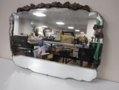 An early 20th century frameless bevel edge mirror surmounted with a carved oak panel