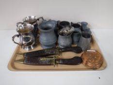 A tray containing two Eastern knives in sheathes, brass mould, plated twin handled tankards,