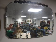 An early 20th century frameless bevel edge mirror surmounted with a carved oak panel