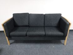 A blonde oak framed three seater settee upholstered in a black fabric