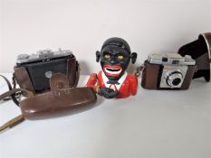 A cast metal money box together with two cameras in leather cases