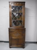 A carved oak corner cabinet with leaded glass door