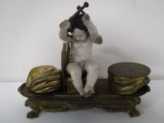 An antique brass desk stand in the form of a cherub playing drums