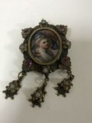 An antique gilt metal pendant/brooch with panel depicting a lady wearing a hat