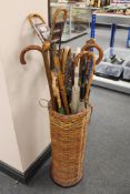 A wicker cylindrical stick stand, containing a quantity of umbrellas, two shooting sticks,
