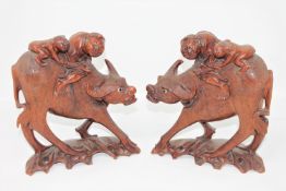 A pair of early 20th century Burmese carved hardwood figures of water buffalo, with riders,