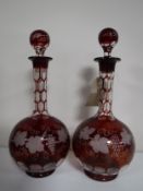 A pair of cranberry glass decanters with leaf and grape decoration.