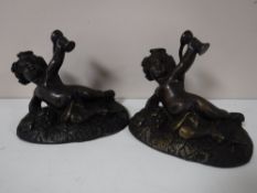 A pair of bronze figures of reclining cherubs holding goblets
