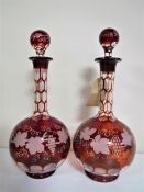 A pair of cranberry glass decanters with leaf and grape decoration.