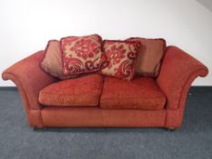 A contemporary scroll arm settee upholstered in a red fabric with loose cushions