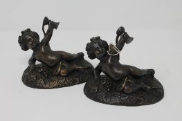 A pair of bronze figures of reclining cherubs holding goblets